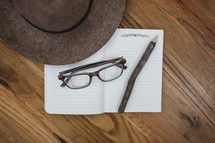 reading glasses, hat, pencil, and notebook on a wood floor 