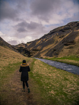 a woman walking on a path beside a mountain stream 