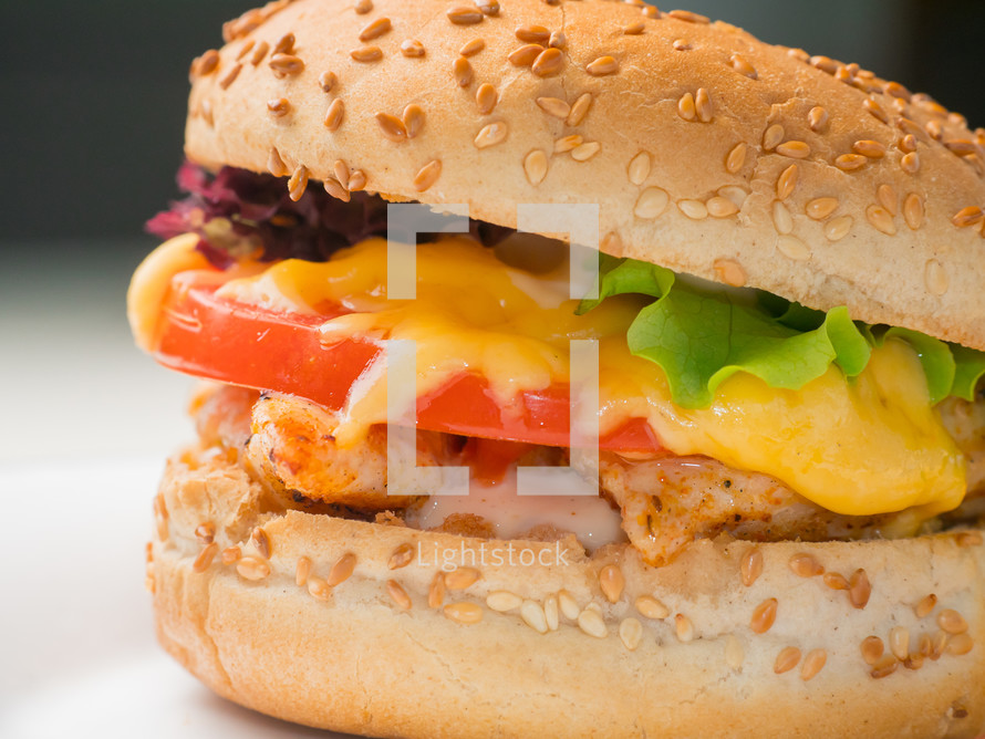 Large chicken sandwich with tomato, lettuce, cheese, and mayo on a sesame bun.