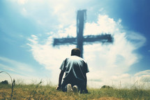 Silhouette of a young man on the grass and praying at the cross