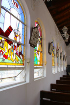 Stained glass windows and wooden pews in a church sanctuary.