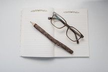 reading glasses and carved pencil on a notebook 