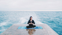 Meditation. Yoga young calm brunette woman by the waves sea on pier relaxing in serene zen. lotus yoga pose on a beach at cloudy weather. Beautiful colorful background.
