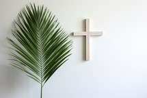 Wooden cross and palm leaf on white wall. Copy space.