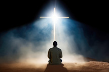 Young man sitting, praying and looking at a cross in the dark