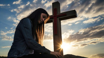 Young woman praying with a cross in the background at sunset. Christian concept.