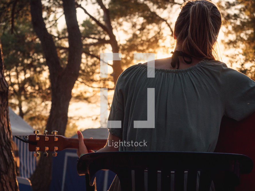 a girl plays guitar at sunset