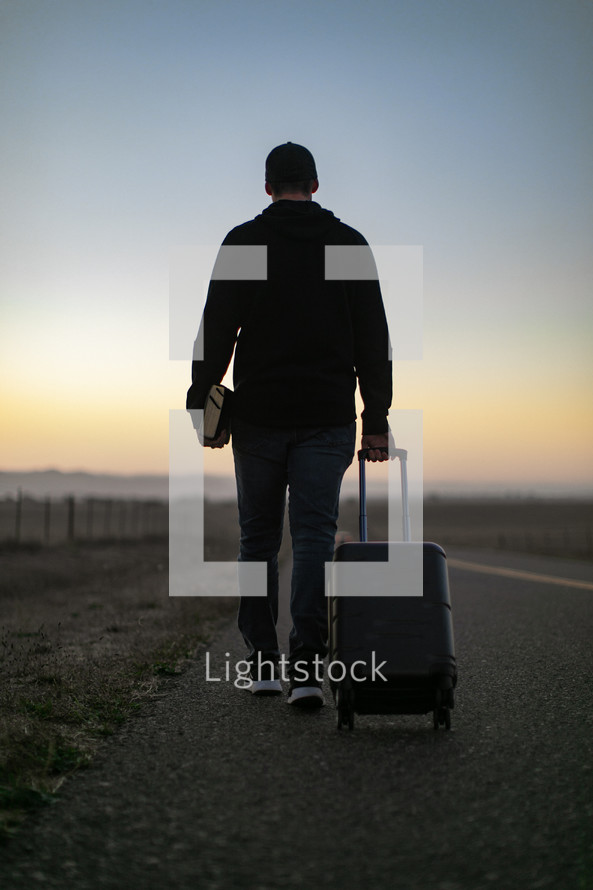 a man walking down a road carrying luggage 