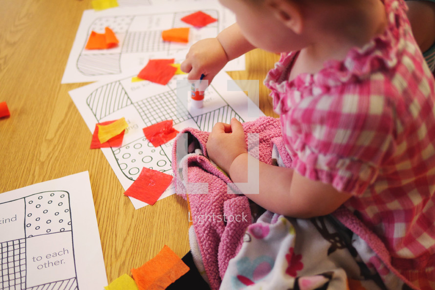 child playing with cut paper and a glue stick 