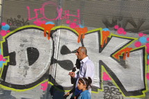 father and daughter walking in front of a graffiti covered wall 