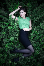 Ophelia; woman in green shirt and black skirt lying on a bed of green plants.