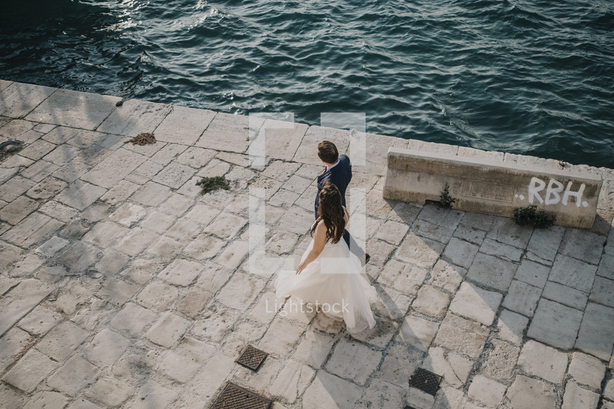 bride and groom walking along a shore 