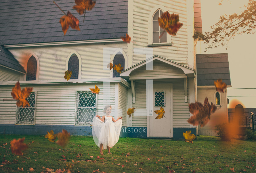 girl in a dress playing in fall leaves in front of a church 