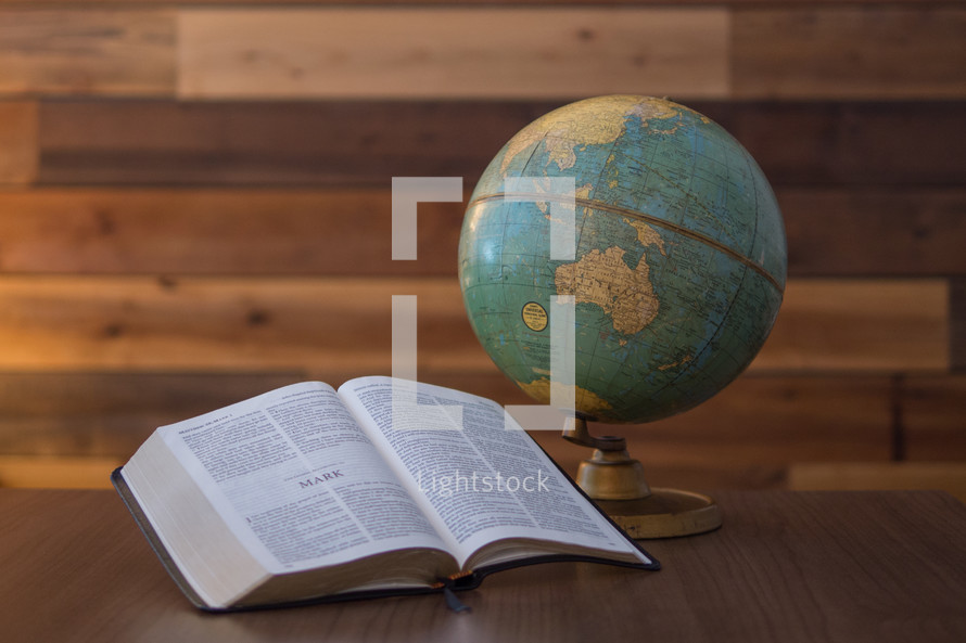 A Bible opened up to the great commission in front of a vintage globe. 