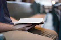 man reading a Bible sitting in a church pew 
