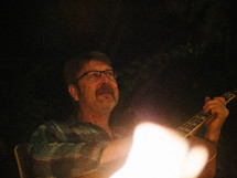 a man playing a guitar by a campfire 