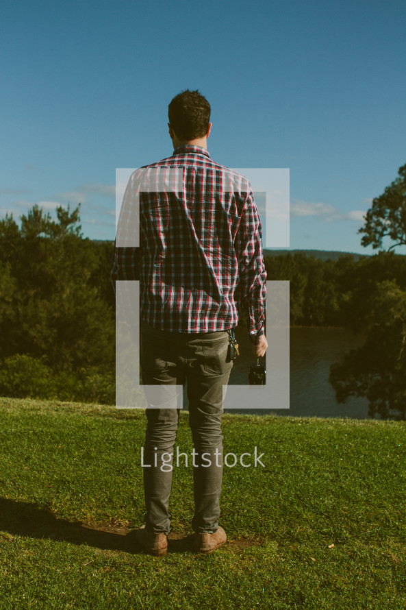 man in a plaid shirt holding a camera at his side