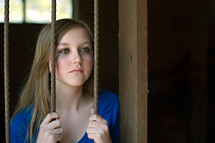 teen girl hiding behind bars with tears in her eyes 