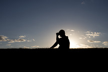silhouette of a boy child sitting in the grass praying 