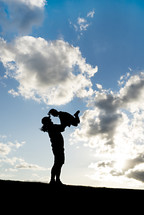 silhouette of a mother holding up her child outdoors 