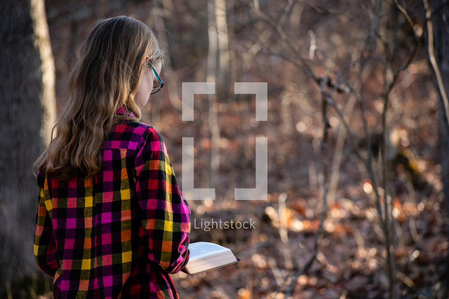 a girl walking outdoors reading a Bible 