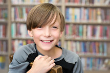 Smiling boy sitting in a chair in a library.