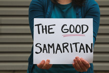A woman holding a sign that reads the Good Samaritan 
