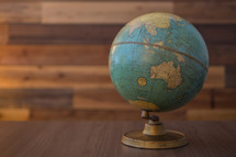 Vintage globe sites on table with wood backdrop.