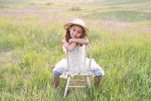 a smiling little girl sitting in a chair in a field 