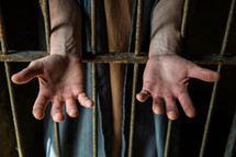 Hands held outstretched through prison bars.