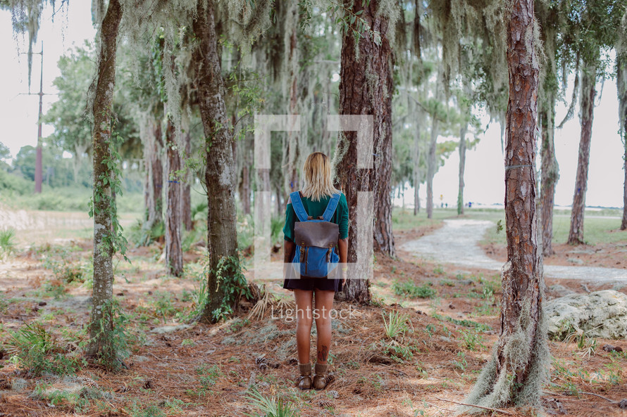 young woman with a backpack standing off a trail 