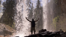 Man standing under a waterfall with arms raised to the sky.
