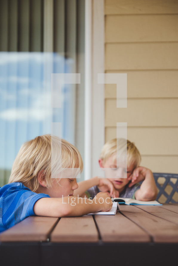 boys reading books outdoors at a table 