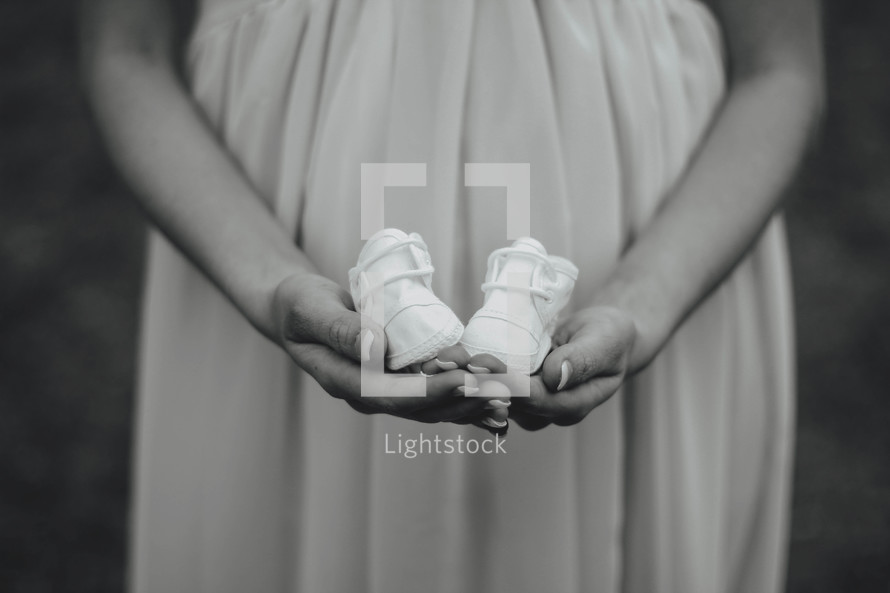 pregnant woman holding baby shoes 