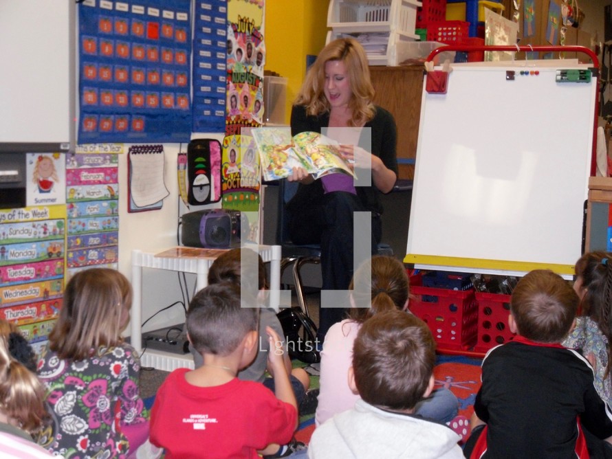 A teacher reading a story book to her kindergarten classroom 
