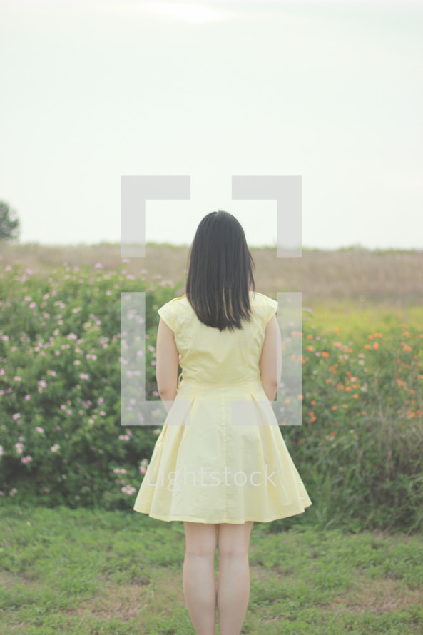 a young woman in a yellow dress standing with her back to the camera 