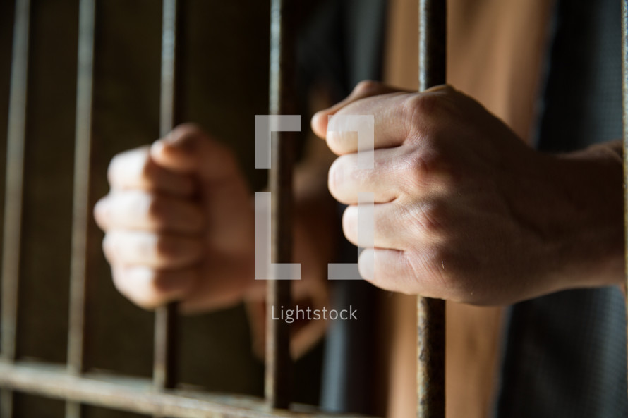A man holding onto prison cell bars.