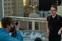 A photographer taking a picture of a smiling young man on a rooftop.