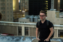 A young man stands on a rooftop with his hands in his pockets.