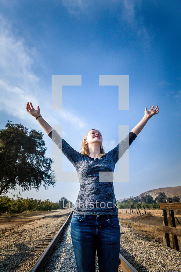 woman with hands raised in worship to God standing on train tracks 