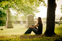 woman sitting in front of a tree in a cemetery 