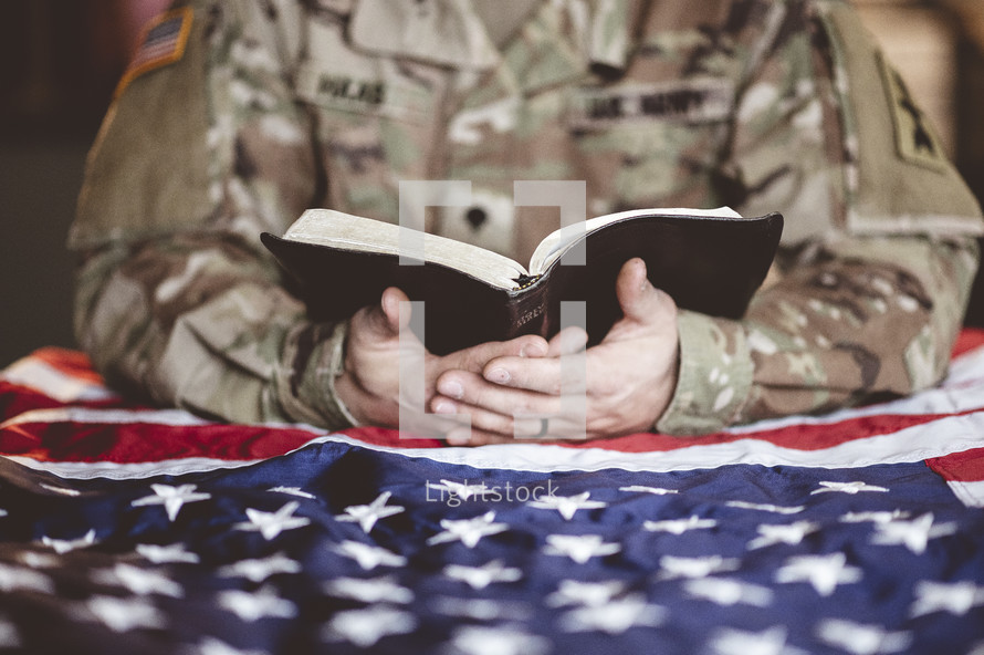 serviceman reading a Bible over an American flag 