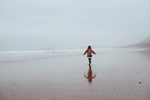 a girl in a coat running on a beach 