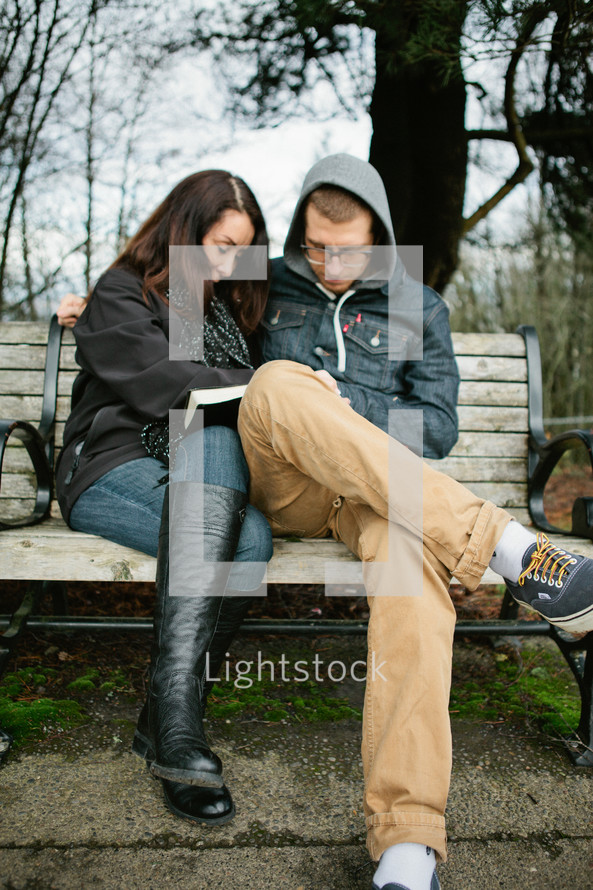 Mother and son praying together while sitting outside on a park bench.