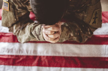 serviceman with head bowed praying over and American flag 