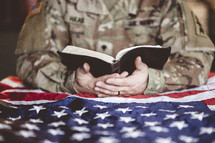 serviceman reading a Bible over an American flag 