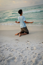 man kneeling in prayer on a beach 