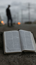 a BIble on a curb and a man standing in the distance 