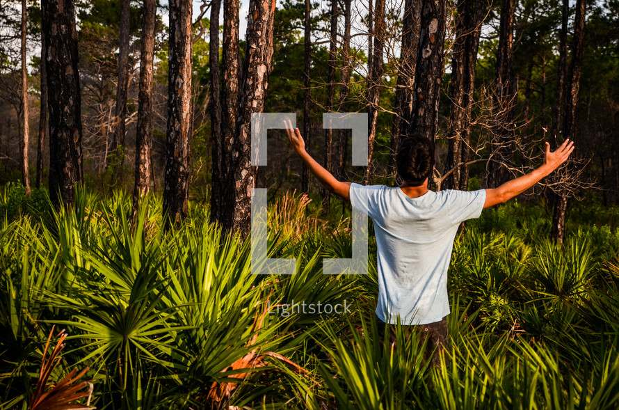 man standing in a field of palms with his hands raised 