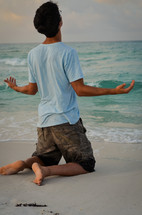 man on his knees in prayer to God on a beach